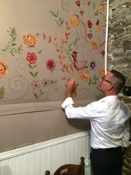 Pascal Jaouen, le célèbre brodeur quimpérois signe sa grande tapisserie qui couvre le mur de la salle de la crêperie du Frugy